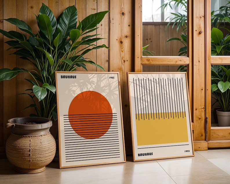 two framed artworks with minimalist designs, placed on a wooden floor next to a potted plant.
