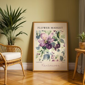 a framed poster of a purple flower on a wall, with a wicker chair and a small table with a plant in the foreground.