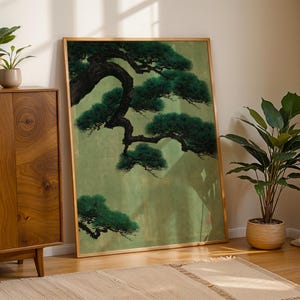 May include: A large rectangular framed wall art piece featuring a detailed painting of a dark green pine tree branch with textured needles against a muted light green background, encased in a thin metallic gold frame with a reflective glass surface.