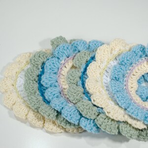 May include: A set of crocheted doilies in shades of cream, light blue, green, and white. The doilies are layered on top of each other, creating a cascading effect.