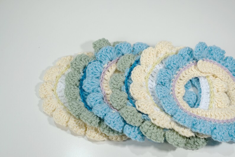 May include: A set of crocheted doilies in shades of cream, light blue, green, and white. The doilies are layered on top of each other, creating a cascading effect.