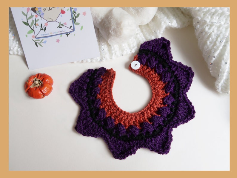 May include: A purple and orange crocheted collar with a white button. The collar is in the shape of a starburst.