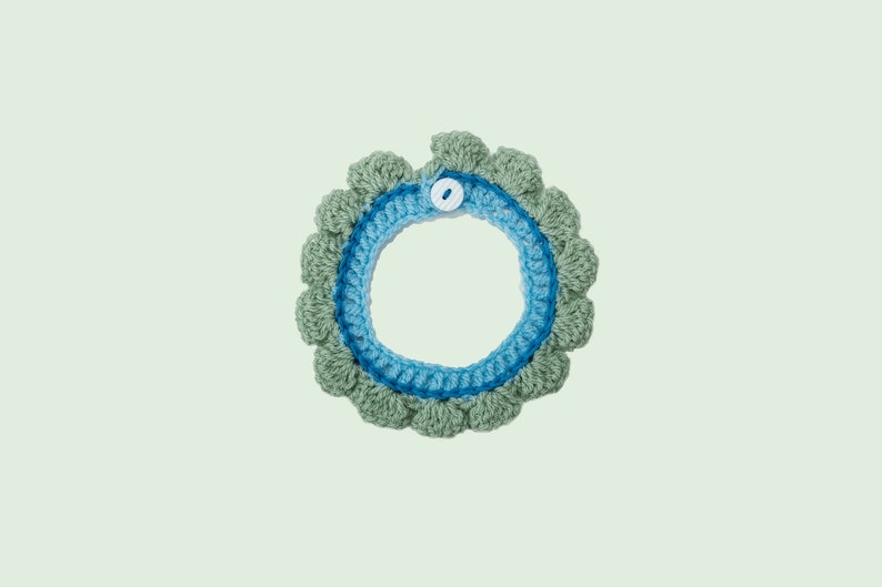 May include: A crocheted collar with a blue and green color scheme. The collar has a white button closure.