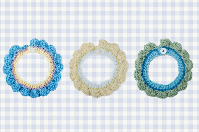 May include: Three crocheted collars in blue, yellow, and green with white buttons. The collars are on a blue and white gingham background.