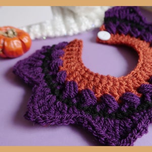 May include: A purple and orange crocheted collar with a white button. The collar is made of yarn and has a scalloped edge.