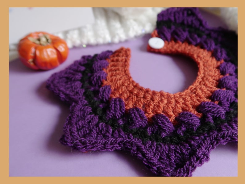May include: A purple and orange crocheted collar with a white button. The collar is made of yarn and has a scalloped edge.
