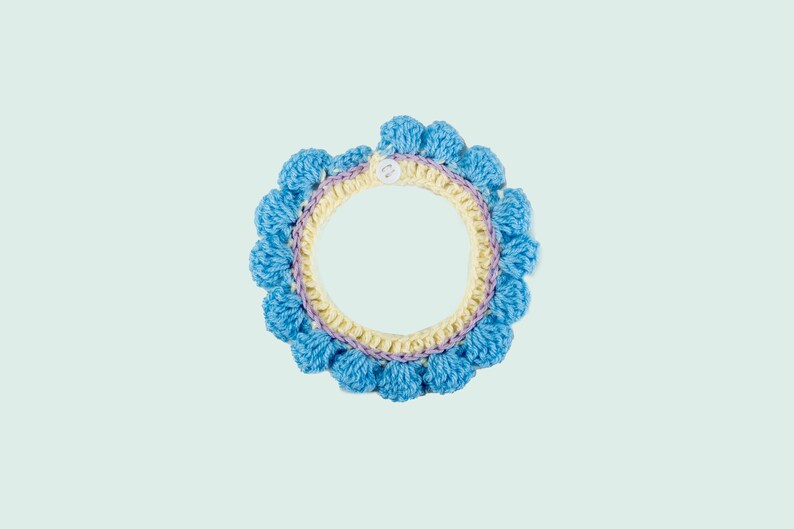 May include: A crocheted collar with a light blue, yellow, and purple design. The collar has a button closure.