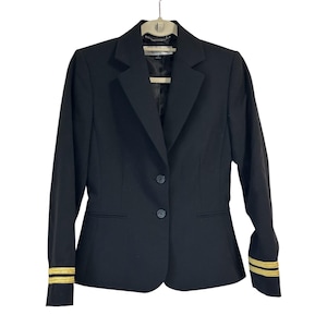 May include: A black blazer with gold stripes on the cuffs. The blazer has a two-button closure and a notched lapel. The jacket is hanging on a hanger.