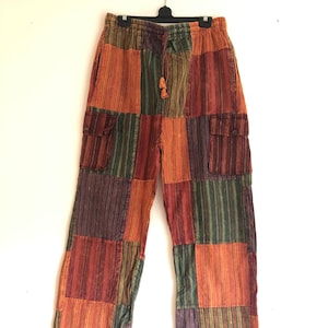 Pode incluir: Calças de patchwork com cintura de cordão e dois bolsos laterais. As calças são feitas de uma variedade de tecidos listrados coloridos em tons de laranja, verde, roxo e marrom.