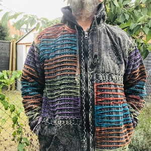 Può includere: Una giacca nera con cappuccio con un design patchwork che presenta strisce colorate e motivi geometrici. La giacca ha una cerniera e un cappuccio con coulisse.