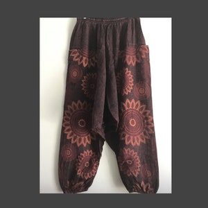 Könnte beinhalten: Braune Baumwollhose mit Blumenmuster. Die Hose hat eine weite Beinweite und einen Bund mit Kordelzug.