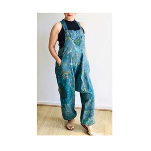 Op de afbeelding: Tie-dye blauwe denim overall met een groen en bruin patroon. De overall heeft een wijde pijp en een ontspannen pasvorm.