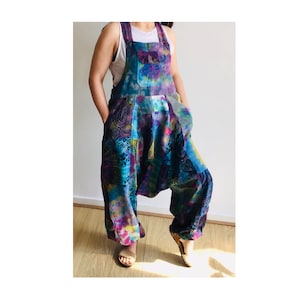 May include: A colourful tie-dye jumpsuit with a patchwork design. The jumpsuit has a wide leg and a loose fit. It features a chest pocket and adjustable straps.