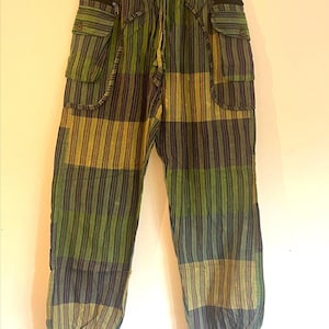 May include: Green, olive, and navy blue striped cargo trousers. They have two large pockets on each leg, a drawstring waist, and elasticated cuffs. The fabric is patterned with vertical stripes.
