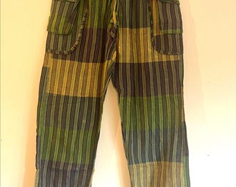 May include: Green, olive, and navy blue striped cargo trousers. They have two large pockets on each leg, a drawstring waist, and elasticated cuffs. The fabric is patterned with vertical stripes.