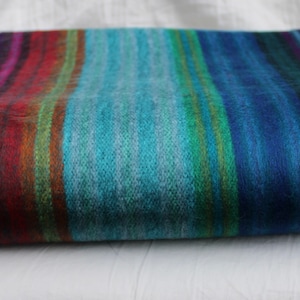 May include: A striped throw blanket featuring a range of colours, including blue, green, red, and purple. The blanket is made from a soft, fluffy material and is ideal for adding a touch of warmth and colour to any room.