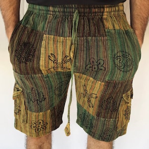 May include: Green, brown and beige patchwork shorts with black printed symbols. The shorts have a drawstring waist and side pockets.