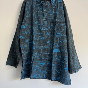 Op de afbeelding: Een lang mouw, donkerblauw shirt met een knoopsluiting en een zak aan de linkerkant. Het shirt heeft een blauwe en witte paddenstoelprint.