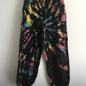 Op de afbeelding: Zwarte sweatpants met een kleurrijk tie-dye patroon. Het patroon heeft tinten roze, geel, blauw en groen.