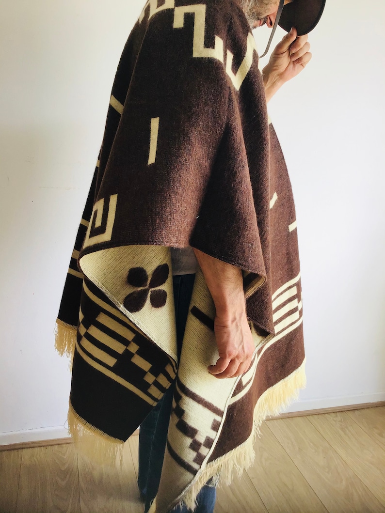 May include: A brown and cream-colored poncho with geometric patterns and fringe. The poncho features a repeating design of rectangles and squares in cream against a brown background. The fringe is a light cream color.