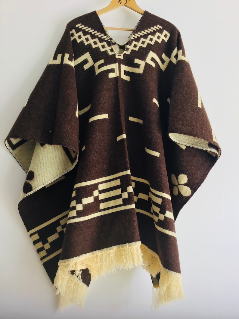 May include: A brown poncho with cream-colored geometric patterns and fringe along the bottom edge. The poncho is made of a thick, woven material and has a V-neck design. The cream-colored pattern includes rectangular and diamond shapes.