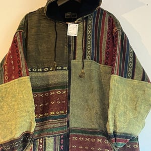 Könnte beinhalten: Eine grüne, braune, rote und blaue Patchwork-Kapuzenjacke mit Reißverschluss. Die Jacke hat ein Fleece-Futter und ein gewebtes Muster.