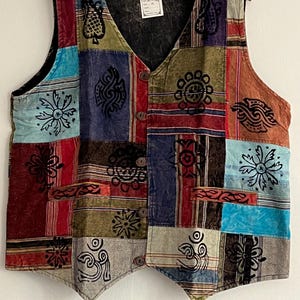 Puede incluir: Un chaleco multi-color de patchwork con cuello en V y cierre de botones. El chaleco está hecho de diferentes telas y presenta varios diseños impresos, incluyendo flores, patrones geométricos y símbolos. El chaleco tiene un aspecto desgastado y está hecho de un material suave y cómodo.