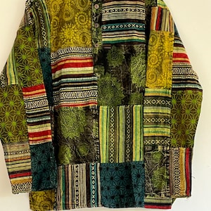 Könnte beinhalten: Ein langärmeliges Patchwork-Hemd mit Stehkragen und einem einzigen Knopfverschluss. Das Hemd besteht aus verschiedenen Stoffen in Grün-, Blau-, Rot- und Brauntönen. Der Stoff hat eine Vielzahl von Mustern, darunter Streifen, geometrische Muster und florale Motive. Das Hemd hat eine lockere Passform und ist perfekt zum Schichten.