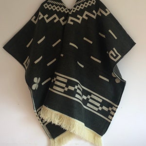 May include: A dark gray poncho with cream-colored geometric patterns and fringe. The poncho features a V-neck and a repeating design of lines, squares, and other shapes. The bottom edge has a cream-colored fringe.