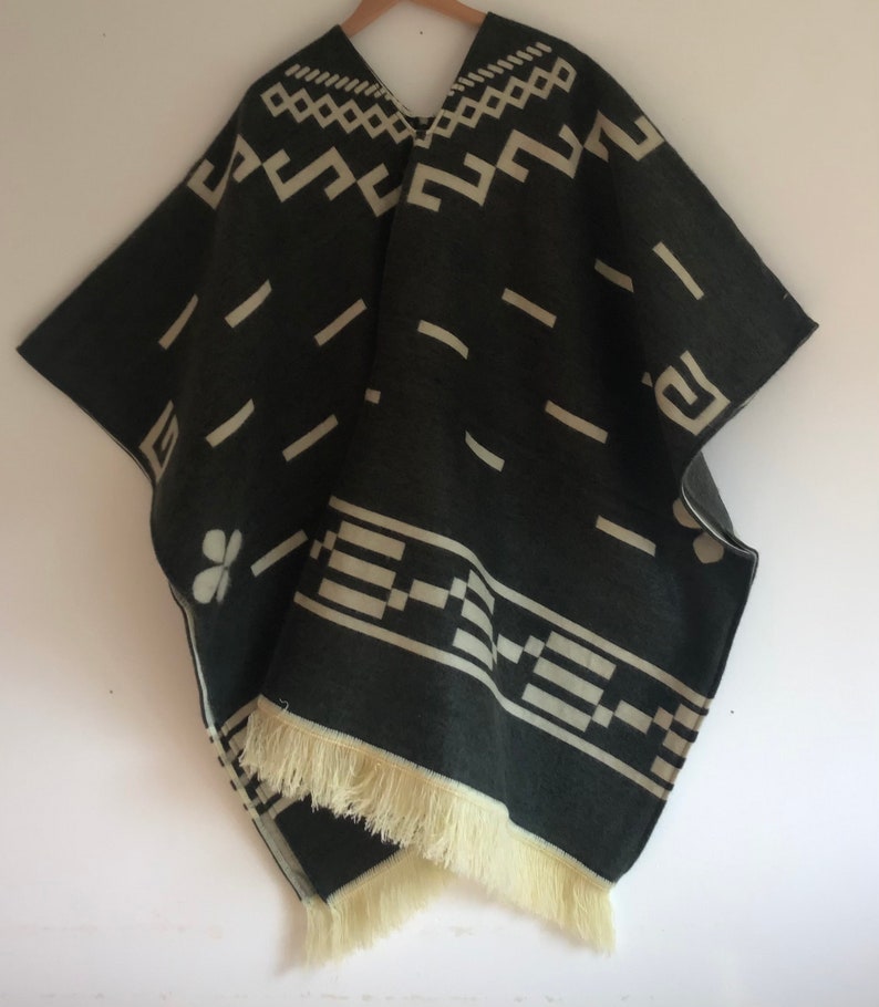 May include: A dark gray poncho with cream-colored geometric patterns and fringe. The poncho features a V-neck and a repeating design of lines, squares, and other shapes. The bottom edge has a cream-colored fringe.