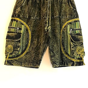 May include: Green and black patterned shorts with two large side pockets. The shorts have a drawstring waist and decorative spiral accents. The pockets feature a green and yellow striped design with a zipper closure. The shorts are hanging on a white background.