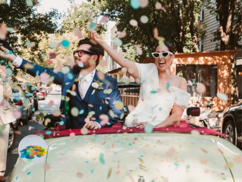 May include: A newly married couple celebrates with confetti in a vintage convertible. The bride wears a white dress and sunglasses, while the groom is in a blue suit. Colorful confetti fills the air, creating a festive atmosphere for a wedding celebration.