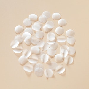 May include: A collection of small, translucent, circular patches scattered on a light beige background. The patches appear to be made of a thin, delicate material, with subtle variations in opacity. The overall effect is soft and airy.