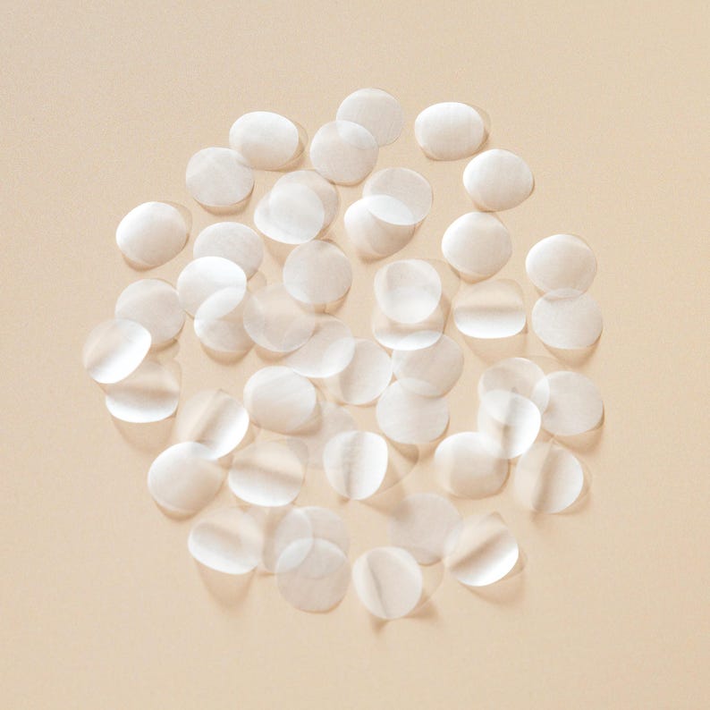 May include: A collection of small, translucent, circular patches scattered on a light beige background. The patches appear to be made of a thin, delicate material, with subtle variations in opacity. The overall effect is soft and airy.