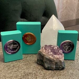 May include: Four teal boxes with gold and silver wax seals, a large clear crystal, and a small purple amethyst crystal. The boxes have the text "Divine Spark Creations" on one of them.