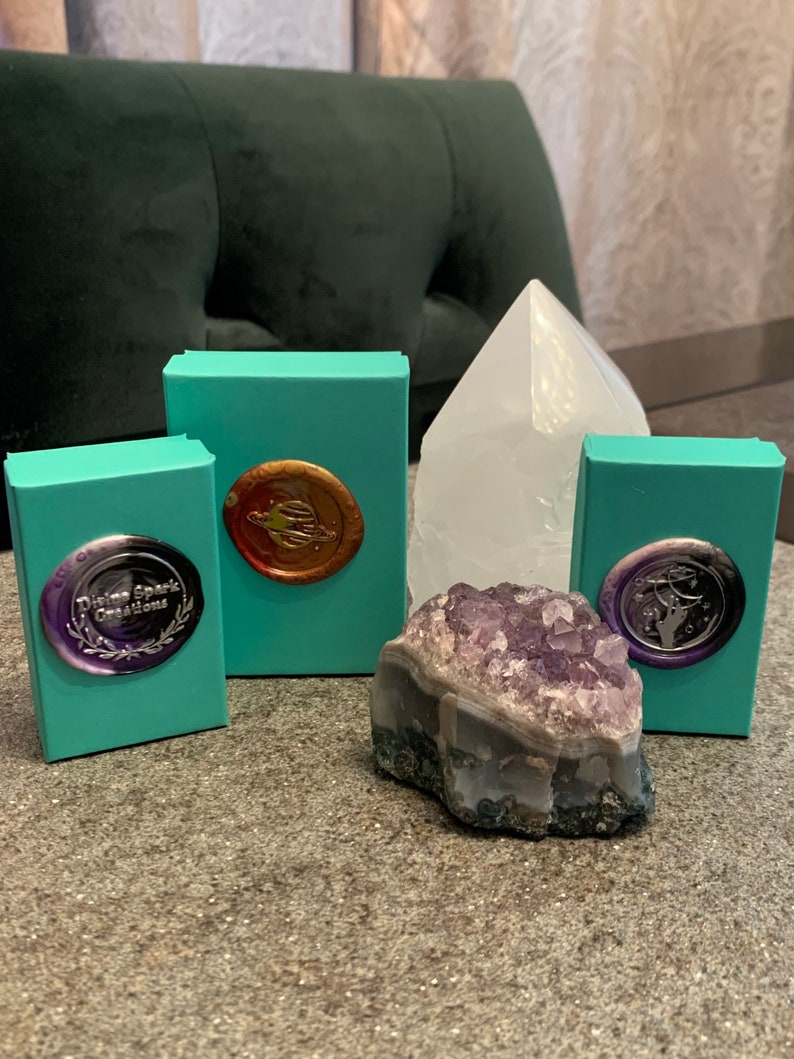 May include: Four teal boxes with gold and silver wax seals, a large clear crystal, and a small purple amethyst crystal. The boxes have the text "Divine Spark Creations" on one of them.