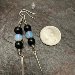 May include: A pair of silver earrings with black and white beads and silver spikes hanging from the bottom. The earrings are shown next to a US quarter for size reference.