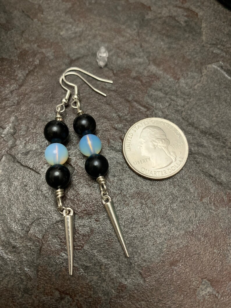 May include: A pair of silver earrings with black and white beads and silver spikes hanging from the bottom. The earrings are shown next to a US quarter for size reference.
