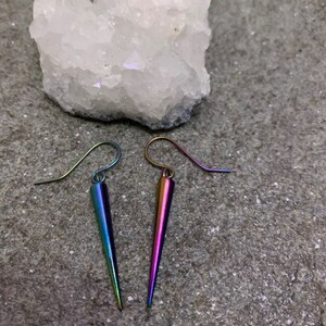 May include: A pair of iridescent earrings with a pointed, teardrop shape. The earrings are made of metal and have a silver-toned hook.