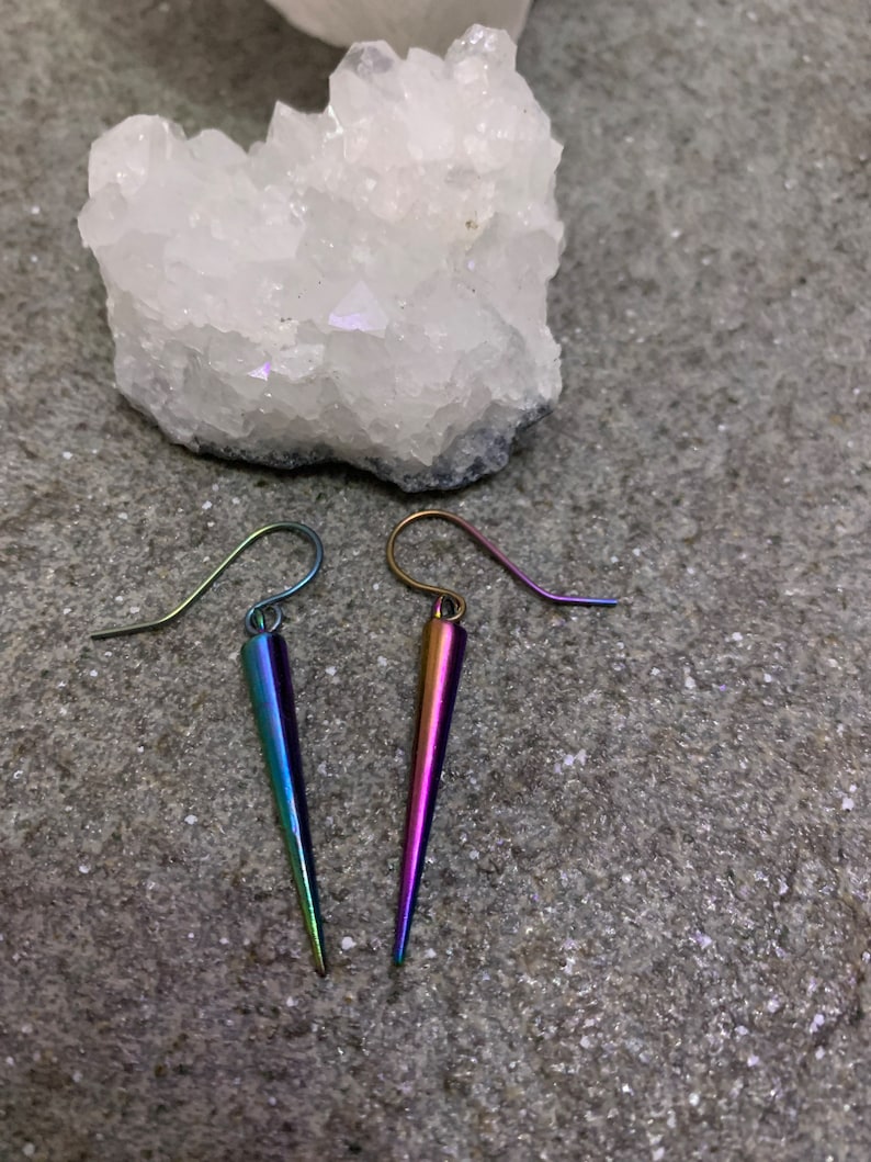 May include: A pair of iridescent earrings with a pointed, teardrop shape. The earrings are made of metal and have a silver-toned hook.