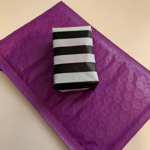 May include: A small, rectangular box wrapped in black and white striped paper. The box is sitting on a purple bubble mailer.