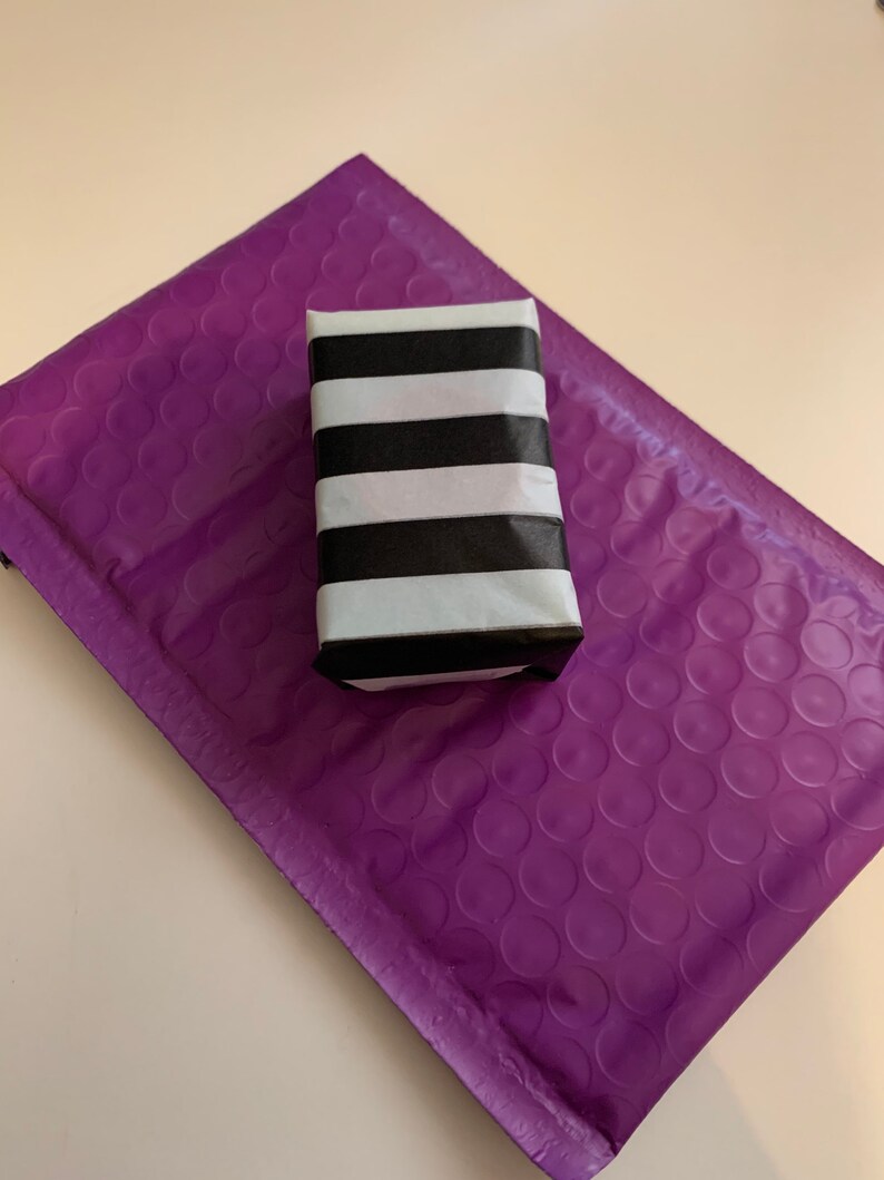 May include: A small, rectangular box wrapped in black and white striped paper. The box is sitting on a purple bubble mailer.