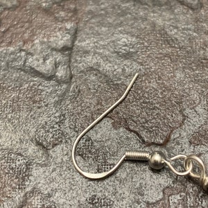 May include: Silver earring hook with a small ball at the end. The hook is made of metal and has a smooth finish.