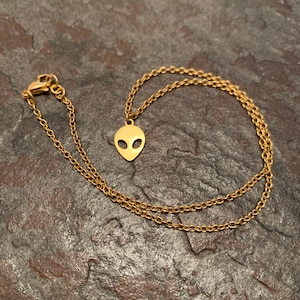 May include: A gold chain necklace with an alien head pendant. The chain is a delicate, linked style.