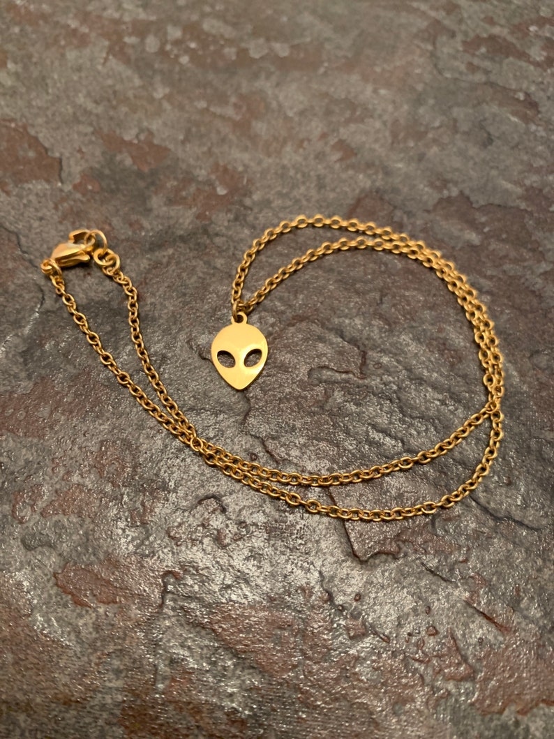 May include: A gold chain necklace with an alien head pendant. The chain is a delicate, linked style.