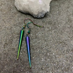May include: A pair of iridescent earrings with a pointed, teardrop shape. The earrings are made of metal and have a silver hook.