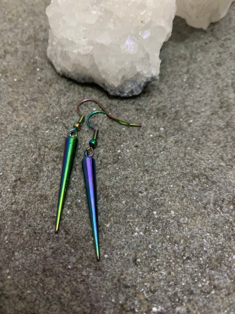 May include: A pair of iridescent earrings with a pointed, teardrop shape. The earrings are made of metal and have a silver hook.