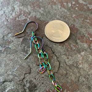 May include: A single iridescent chain earring with a hook closure. The earring is shown next to a US quarter for size comparison.
