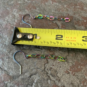 May include: Two rainbow-colored chain earrings with a hook closure. The earrings are measured against a yellow tape measure, showing they are approximately 1 1/2 inches long.
