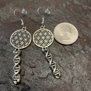 May include: Silver earrings featuring a flower of life design and a DNA helix drop. The earrings are approximately the size of a 25 pence coin.
